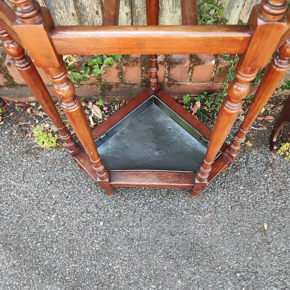 A Victorian mahogany triangular corner umbrella stand featuring turned posts, decorative finials, a compartmentalised top frame, and a dark metal drip tray base. View III