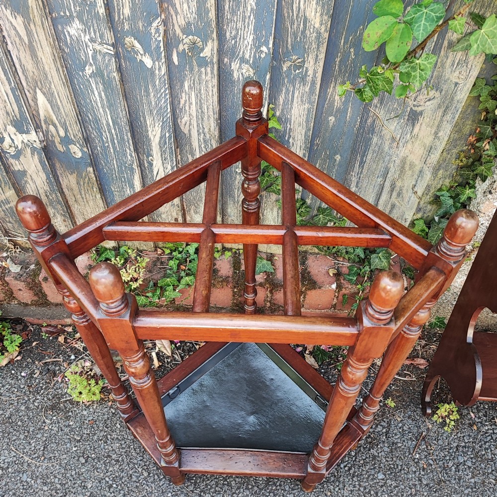 A Victorian mahogany triangular corner umbrella stand featuring turned posts, decorative finials, a compartmentalised top frame, and a dark metal drip tray base. View IV