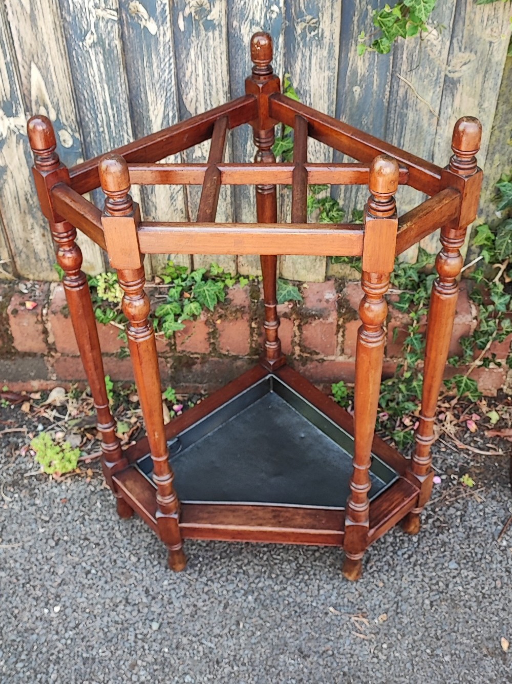 A Victorian mahogany triangular corner umbrella stand featuring turned posts, decorative finials, a compartmentalised top frame, and a dark metal drip tray base. View V