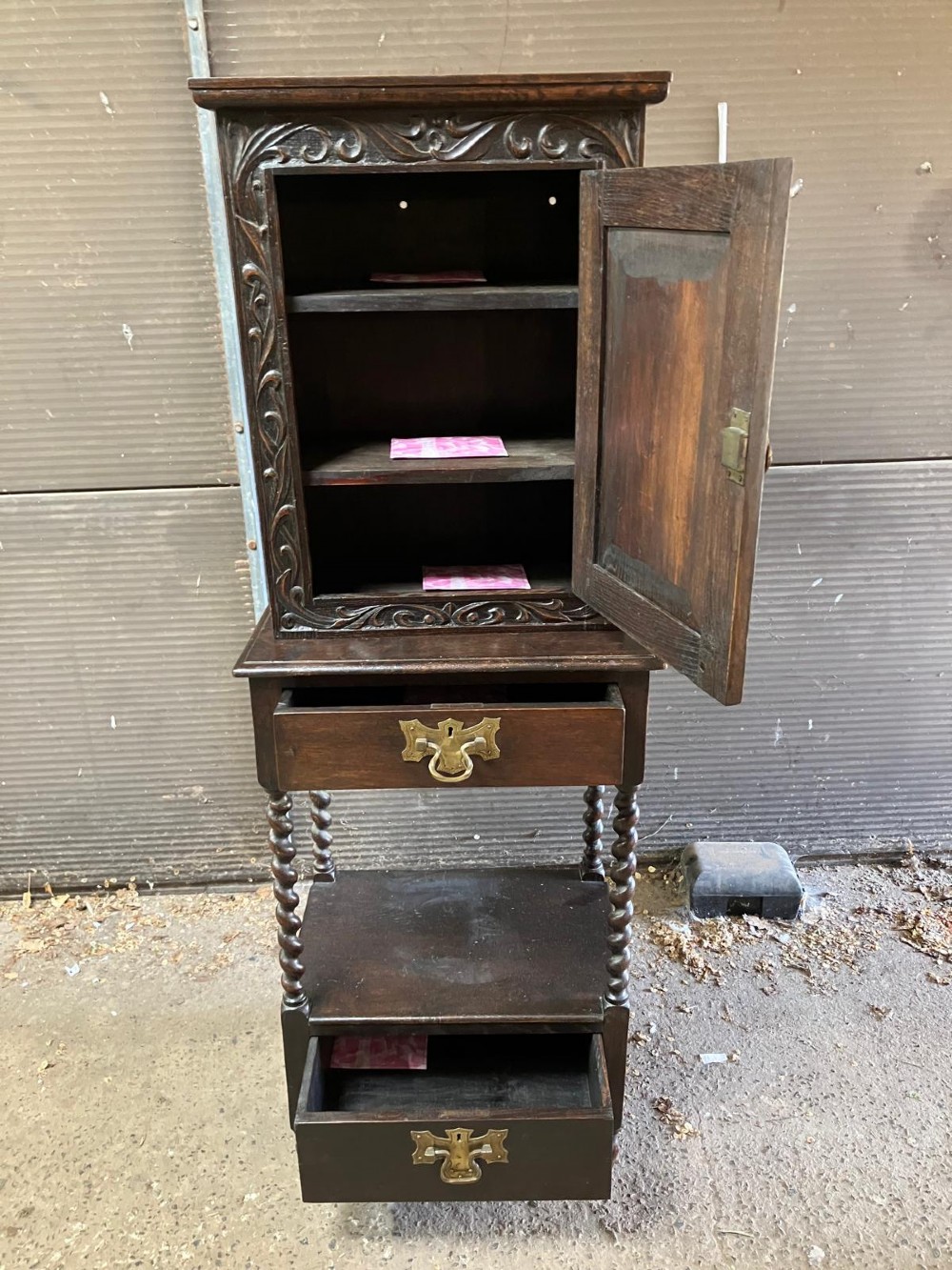 An antique dark carved oak hall cabinet featuring an upper cupboard door with Gothic arched relief carving, two drawers with brass drop handles, and turned barley twist legs. View V