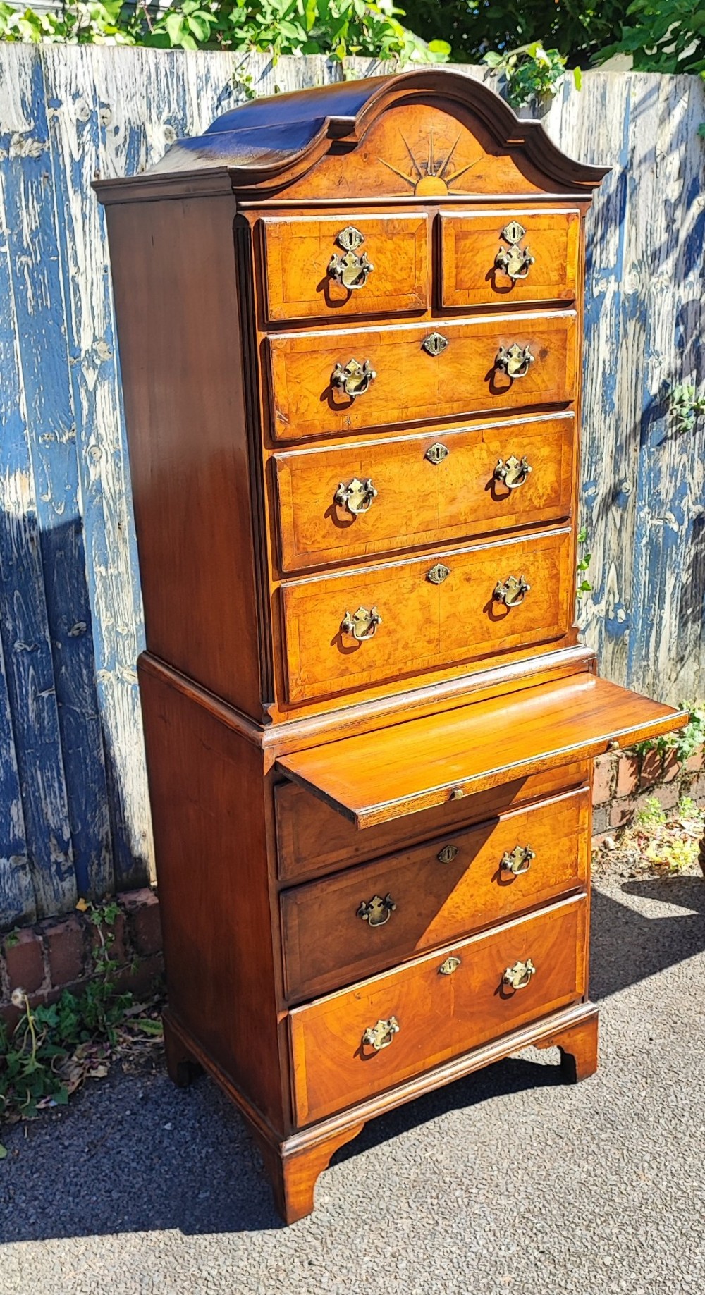 A tall antique walnut chest on chest featuring an arched pediment top with sunburst inlay, brass drop handles, and bracket feet. View IV