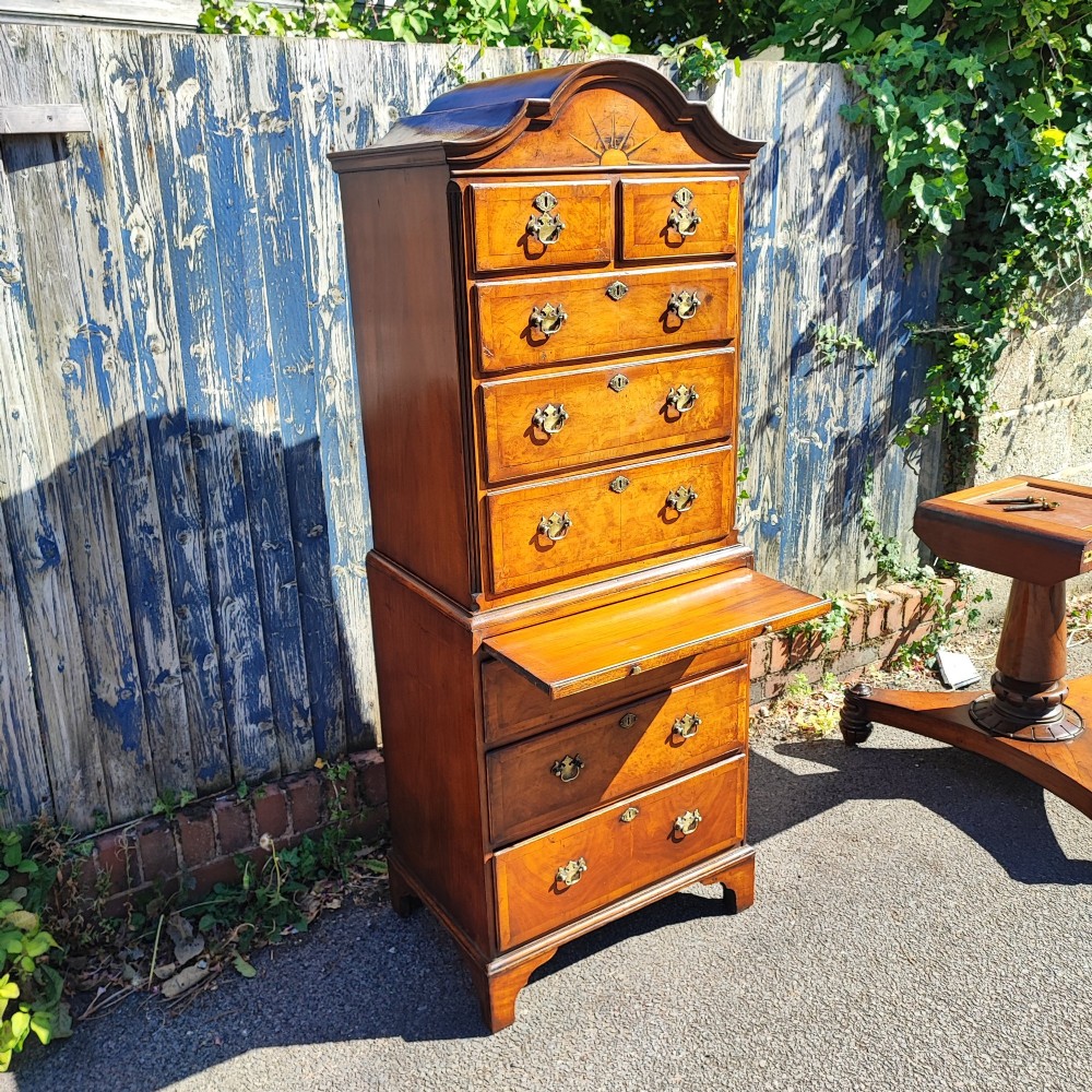 A tall antique walnut chest on chest featuring an arched pediment top with sunburst inlay, brass drop handles, and bracket feet. View V