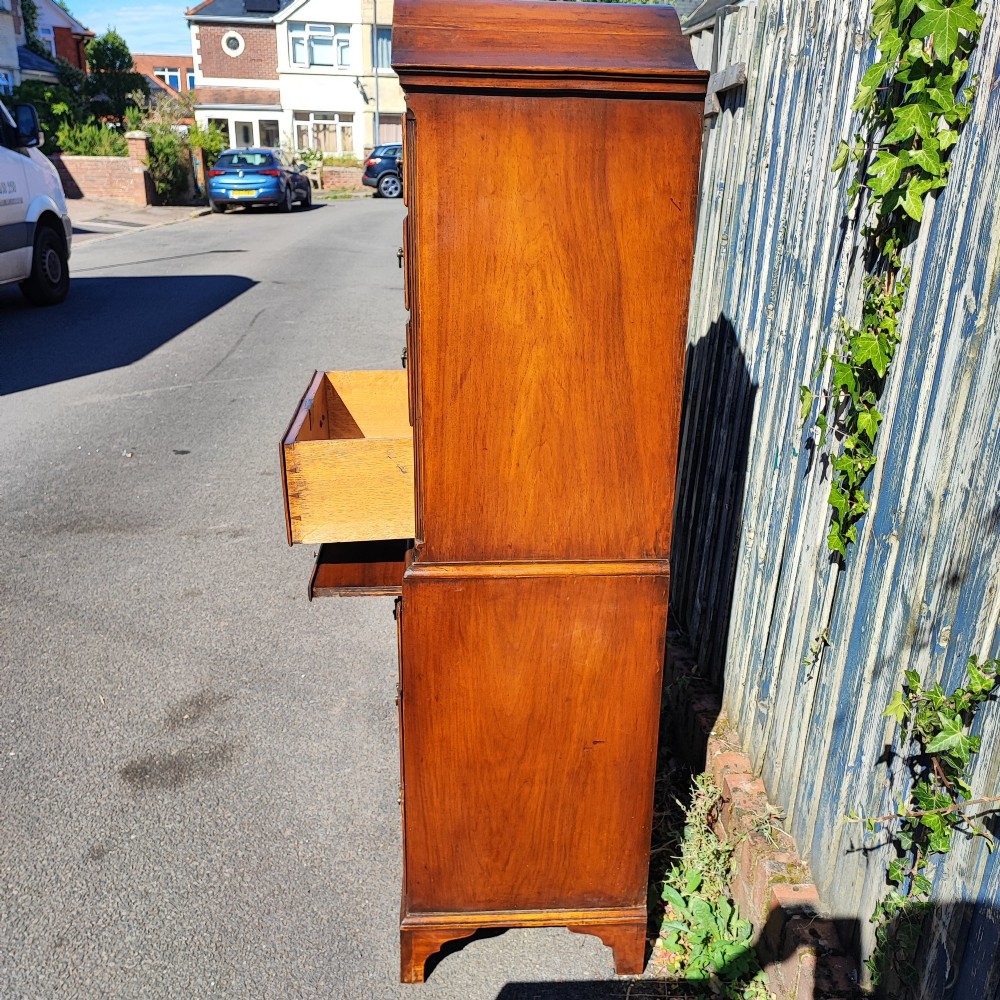 A tall antique walnut chest on chest featuring an arched pediment top with sunburst inlay, brass drop handles, and bracket feet. View X