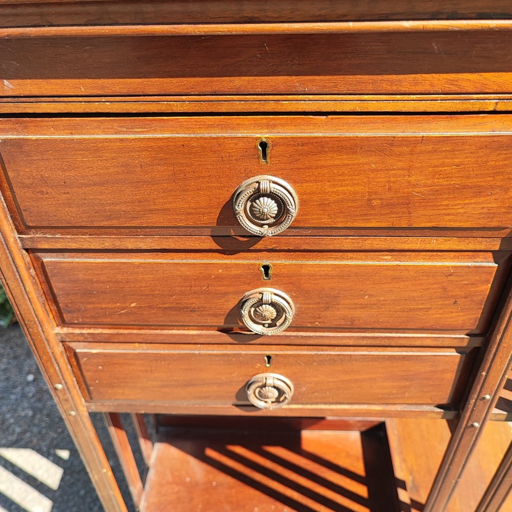 An Edwardian inlaid mahogany revolving bookcase featuring a square top with a central starburst patera inlay, three small drawers with brass ring handles, and vertical timber side slats. View V