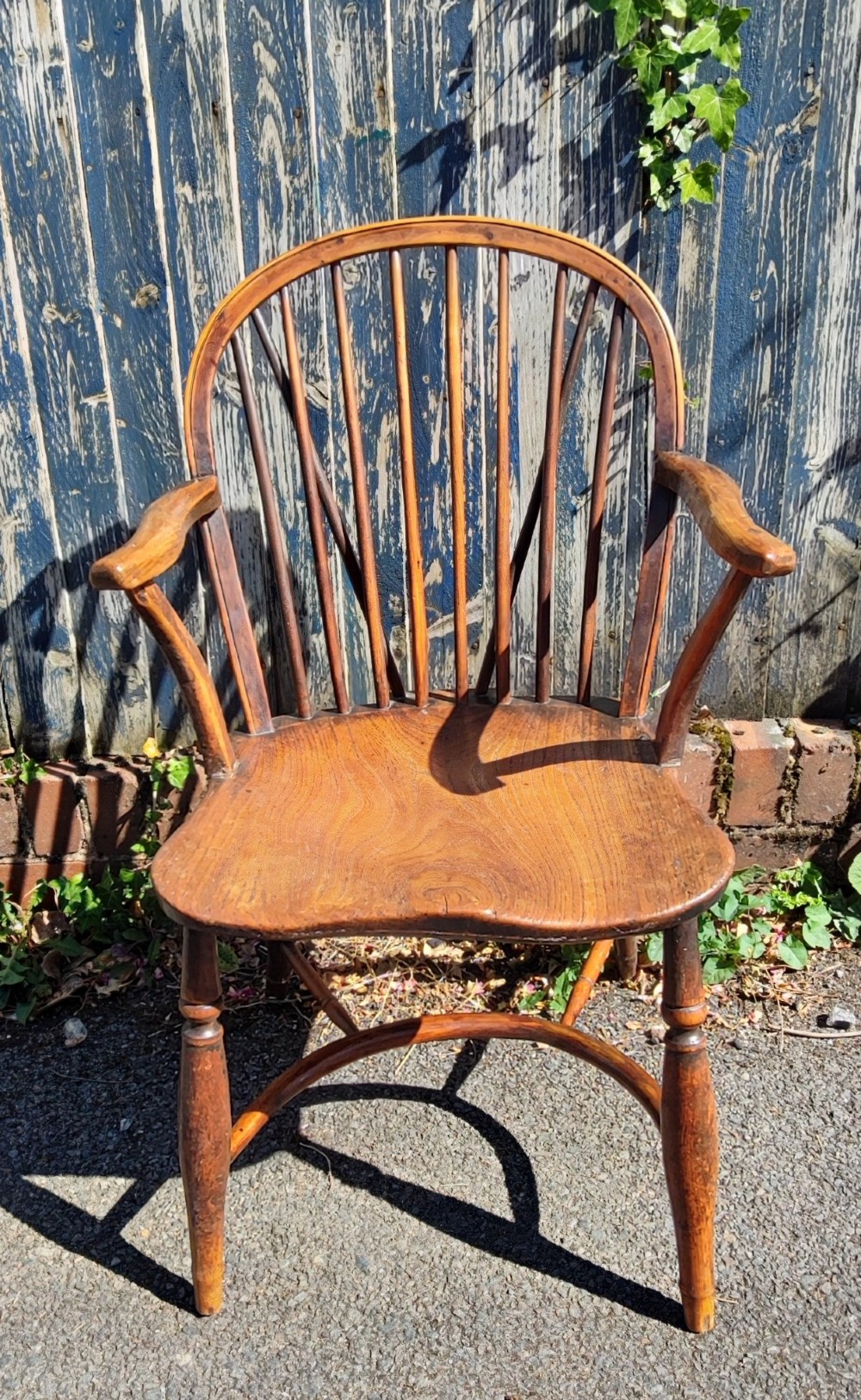 An antique wooden Windsor armchair crafted from yew and elm, featuring a hoop back with thin spindles, curved armrests, a shaped saddle seat, turned legs, and a rounded stretcher. View III
