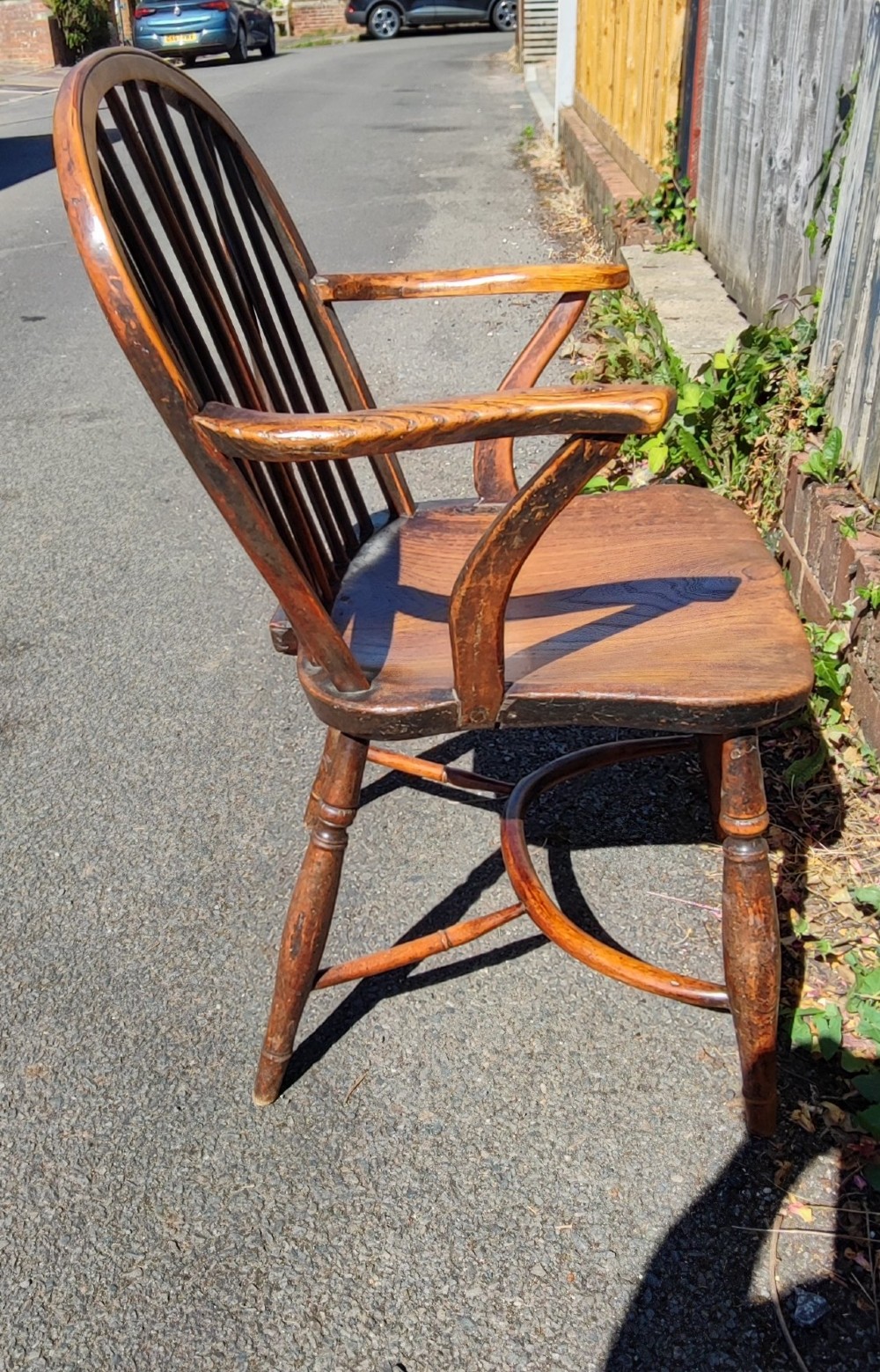 An antique wooden Windsor armchair crafted from yew and elm, featuring a hoop back with thin spindles, curved armrests, a shaped saddle seat, turned legs, and a rounded stretcher. View IV