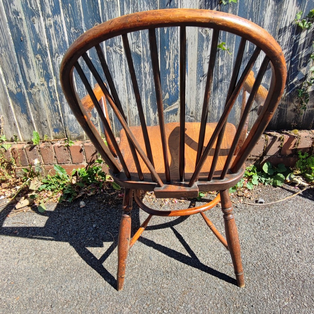 An antique wooden Windsor armchair crafted from yew and elm, featuring a hoop back with thin spindles, curved armrests, a shaped saddle seat, turned legs, and a rounded stretcher. View V