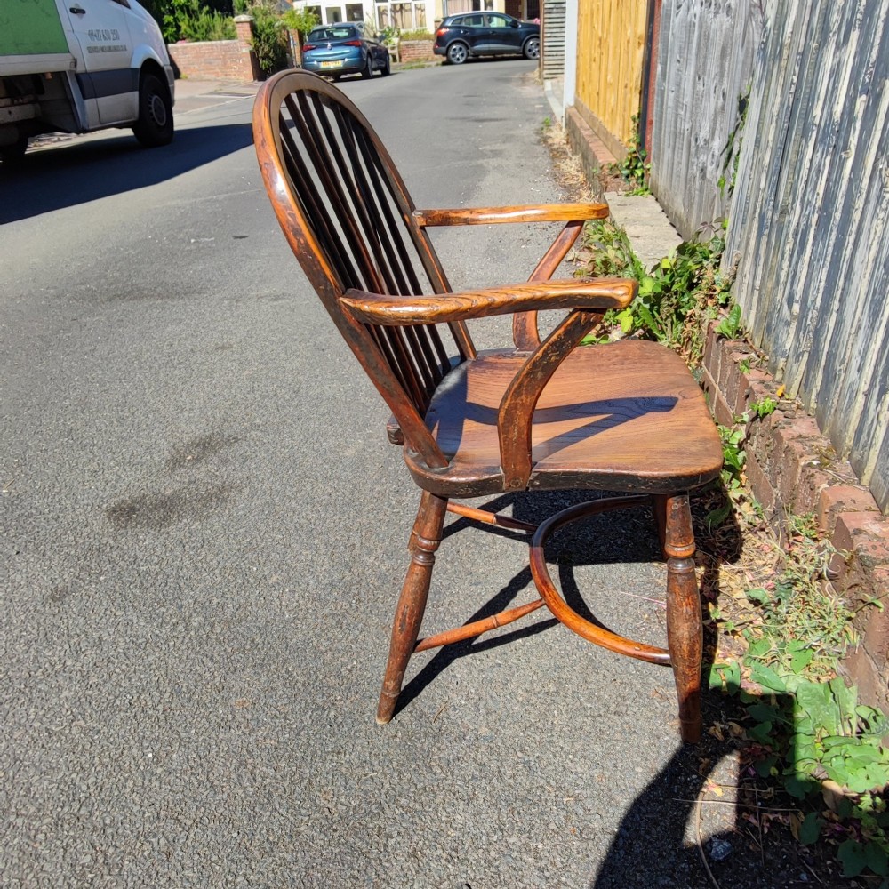 An antique wooden Windsor armchair crafted from yew and elm, featuring a hoop back with thin spindles, curved armrests, a shaped saddle seat, turned legs, and a rounded stretcher. View VI