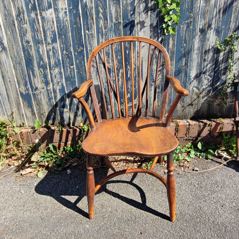 An antique wooden Windsor armchair crafted from yew and elm, featuring a hoop back with thin spindles, curved armrests, a shaped saddle seat, turned legs, and a rounded stretcher. View VII
