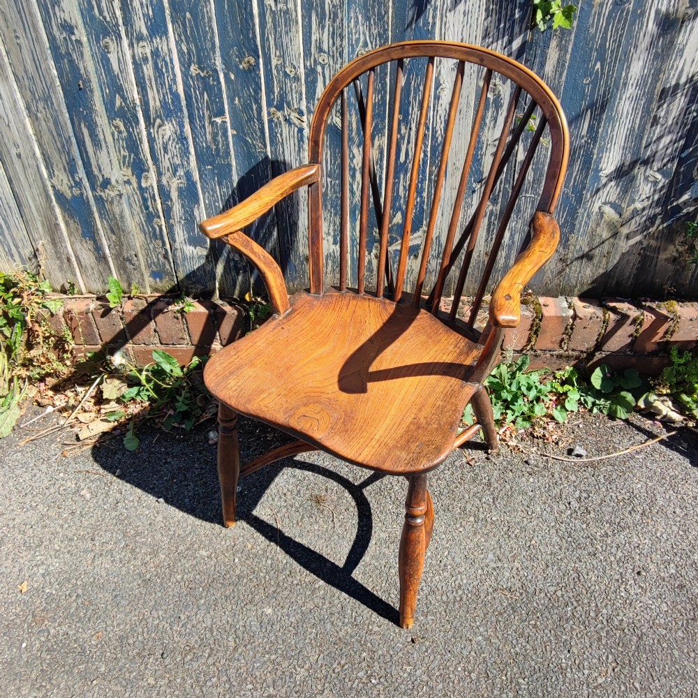 An antique wooden Windsor armchair crafted from yew and elm, featuring a hoop back with thin spindles, curved armrests, a shaped saddle seat, turned legs, and a rounded stretcher. View IX