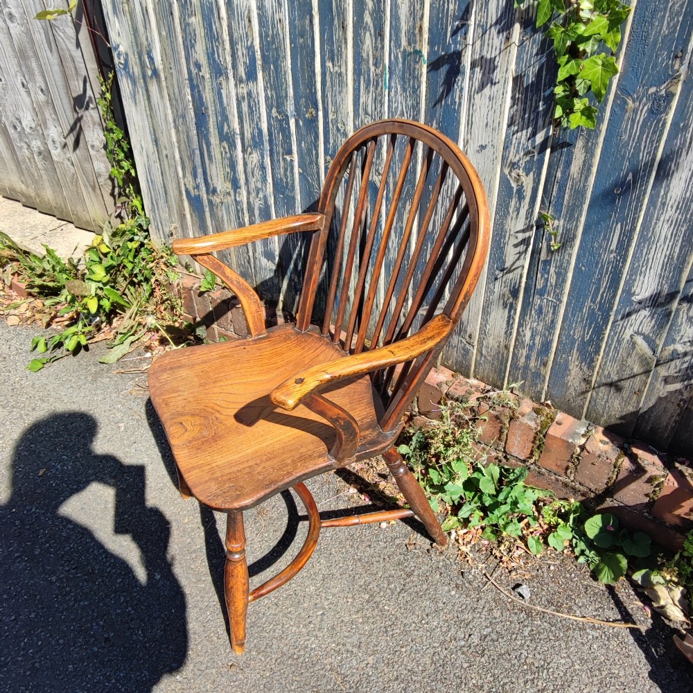 An antique wooden Windsor armchair crafted from yew and elm, featuring a hoop back with thin spindles, curved armrests, a shaped saddle seat, turned legs, and a rounded stretcher. View X