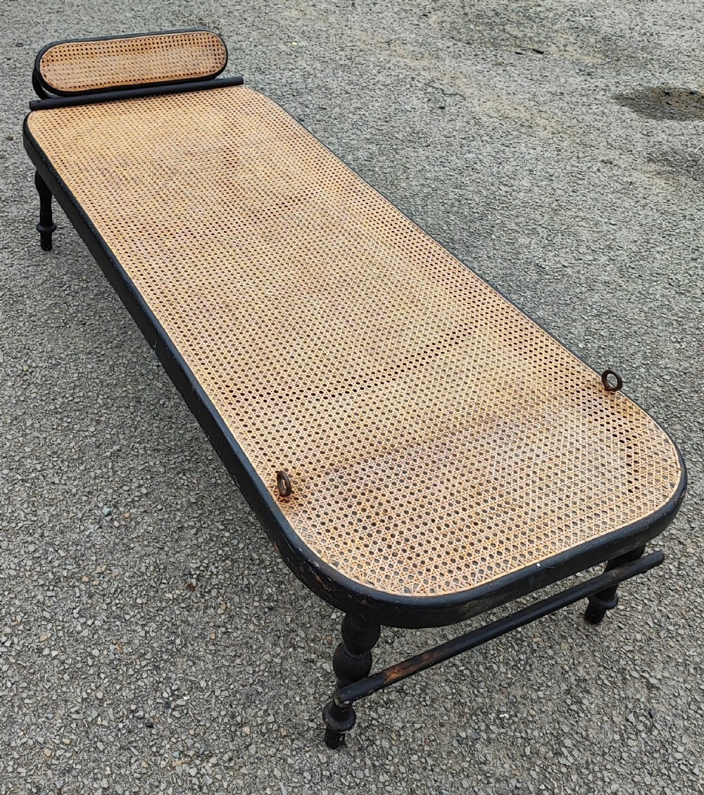 An ebonised wooden daybed with a long hand-woven cane seat, turned legs, and an integrated low headrest.