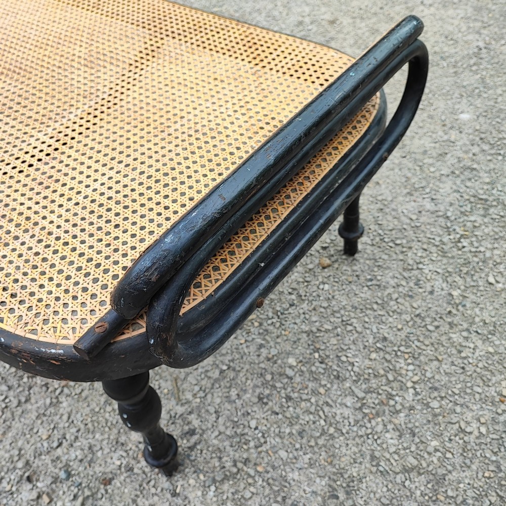 An ebonised wooden daybed with a long hand-woven cane seat, turned legs, and an integrated low headrest. View II