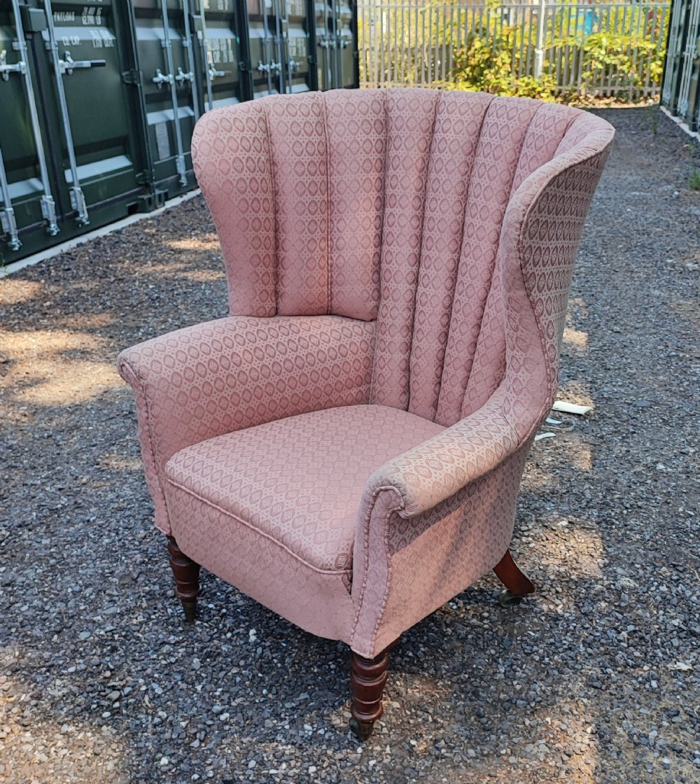 A Regency style barrel back wing armchair upholstered in patterned dusky pink fabric with channel tufting and turned wooden front legs on castors.