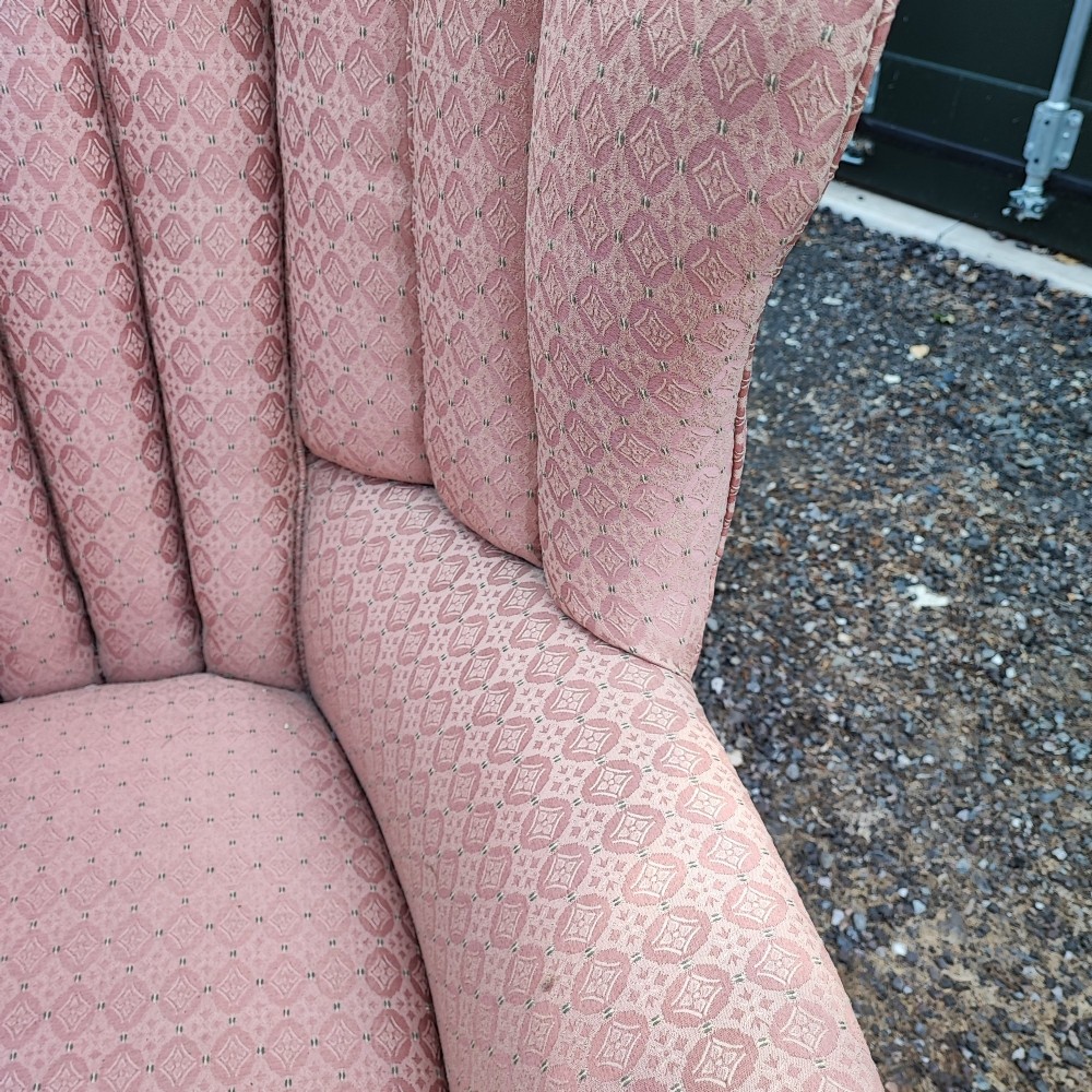 A Regency style barrel back wing armchair upholstered in patterned dusky pink fabric with channel tufting and turned wooden front legs on castors. View II