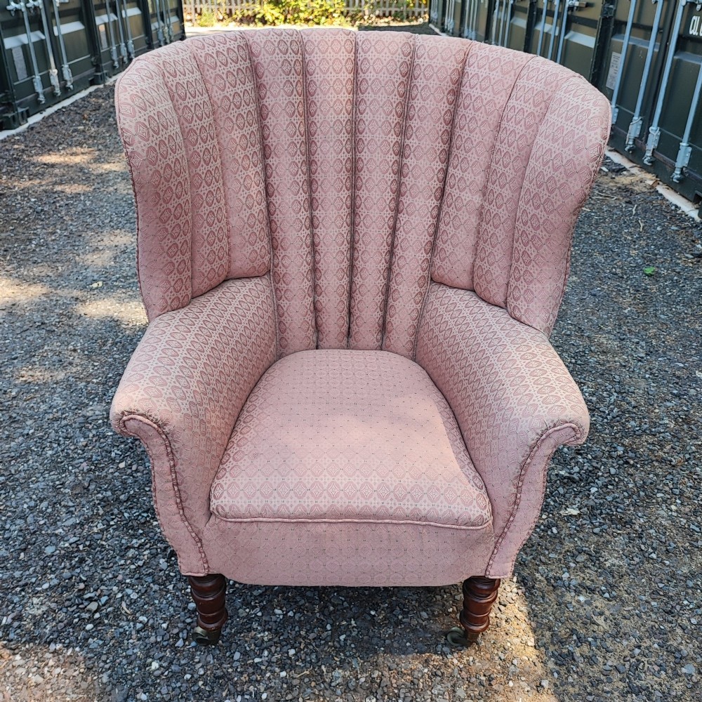 A Regency style barrel back wing armchair upholstered in patterned dusky pink fabric with channel tufting and turned wooden front legs on castors. View III