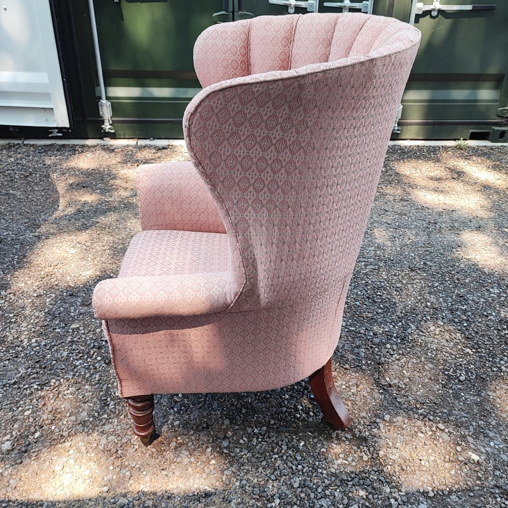 A Regency style barrel back wing armchair upholstered in patterned dusky pink fabric with channel tufting and turned wooden front legs on castors. View IV