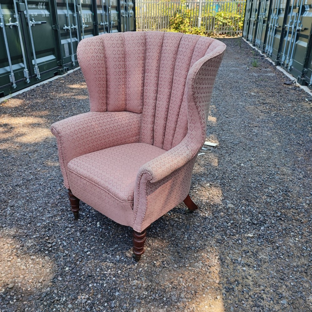 A Regency style barrel back wing armchair upholstered in patterned dusky pink fabric with channel tufting and turned wooden front legs on castors. View V