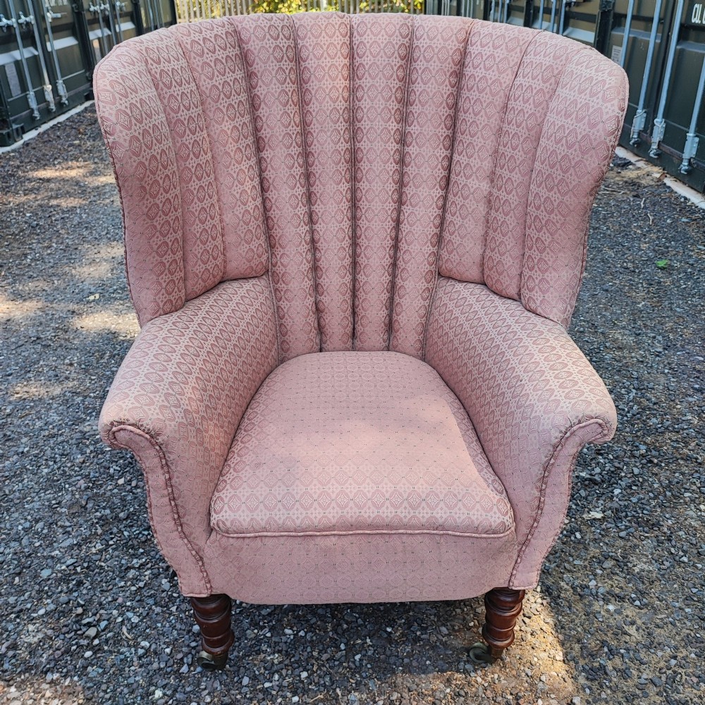 A Regency style barrel back wing armchair upholstered in patterned dusky pink fabric with channel tufting and turned wooden front legs on castors. View VIII
