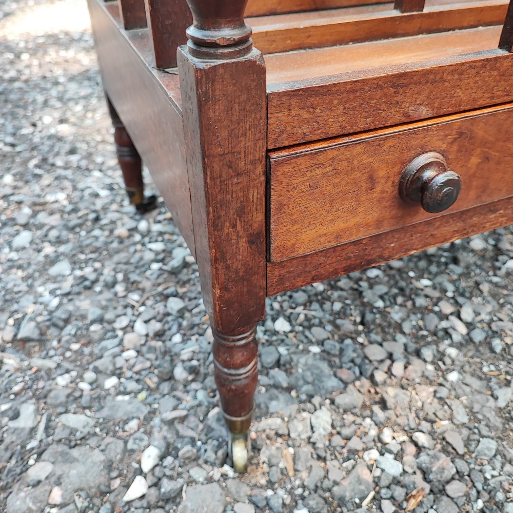 An antique Regency mahogany Canterbury featuring slatted vertical dividers, a central carrying handle, a single base drawer, and turned legs with brass castors. View II