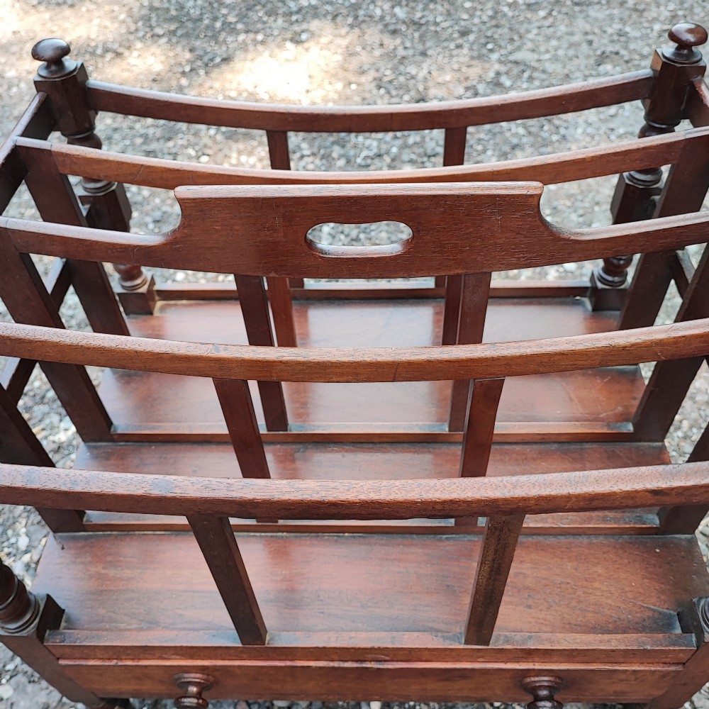 An antique Regency mahogany Canterbury featuring slatted vertical dividers, a central carrying handle, a single base drawer, and turned legs with brass castors. View IV