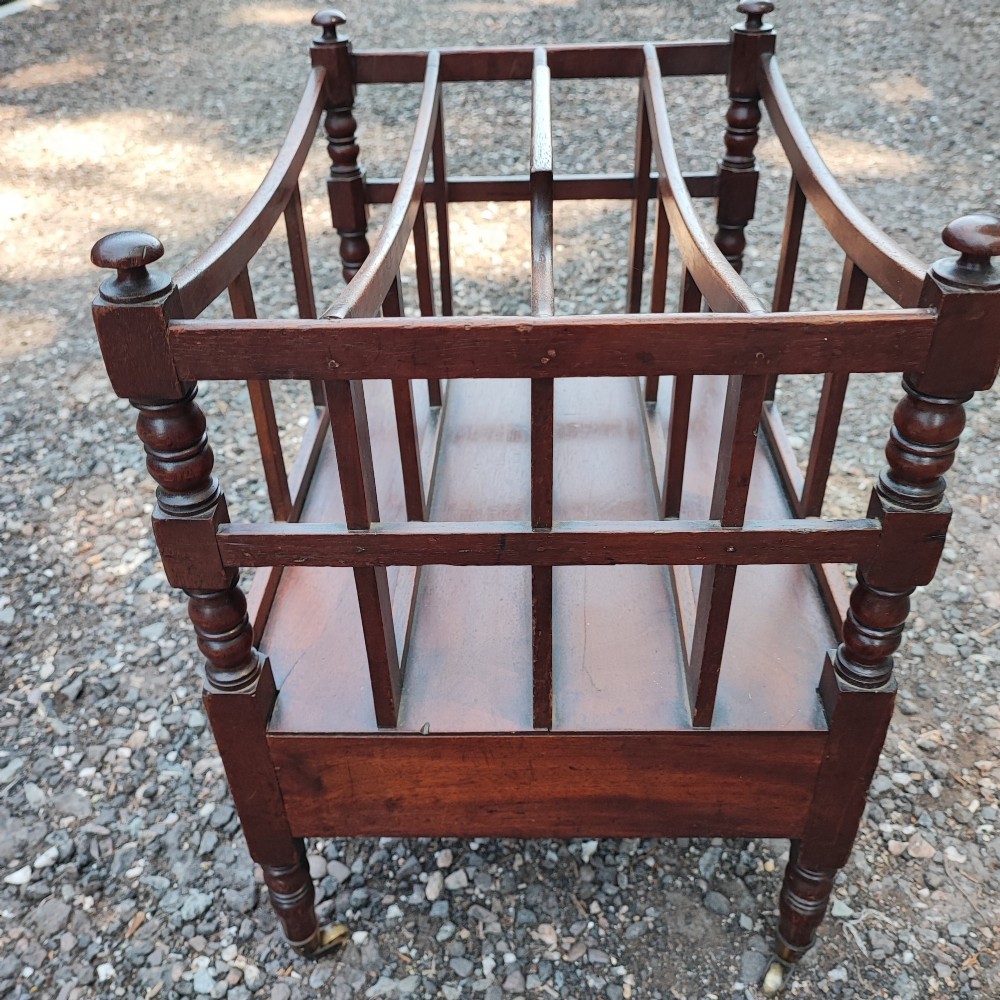 An antique Regency mahogany Canterbury featuring slatted vertical dividers, a central carrying handle, a single base drawer, and turned legs with brass castors. View V