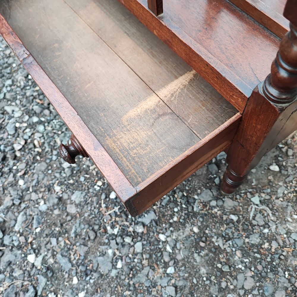 An antique Regency mahogany Canterbury featuring slatted vertical dividers, a central carrying handle, a single base drawer, and turned legs with brass castors. View VI