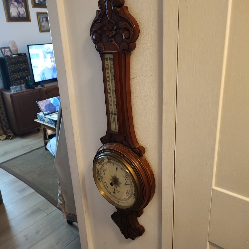 A carved Victorian mahogany aneroid wall barometer featuring top scrollwork, an integrated thermometer trunk, and a circular brass-rimmed dial. View II