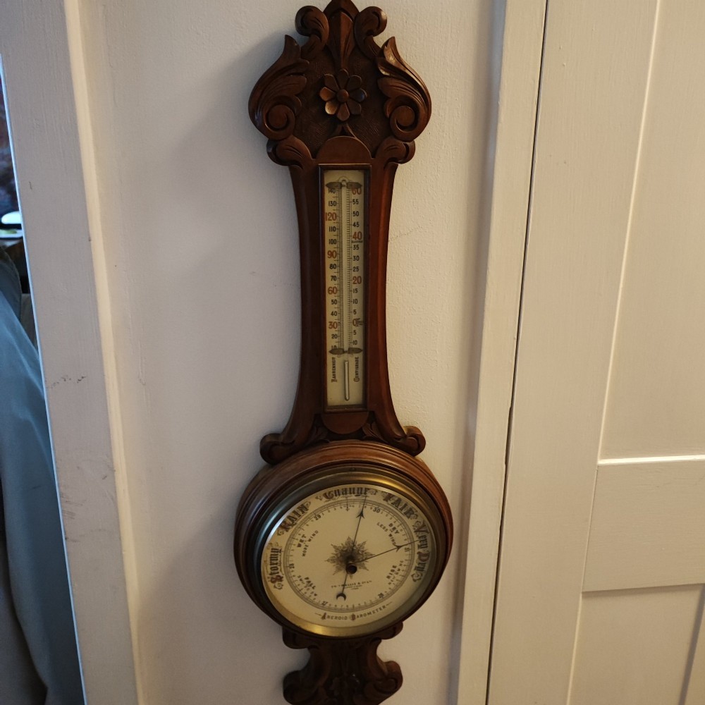 A carved Victorian mahogany aneroid wall barometer featuring top scrollwork, an integrated thermometer trunk, and a circular brass-rimmed dial. View IV