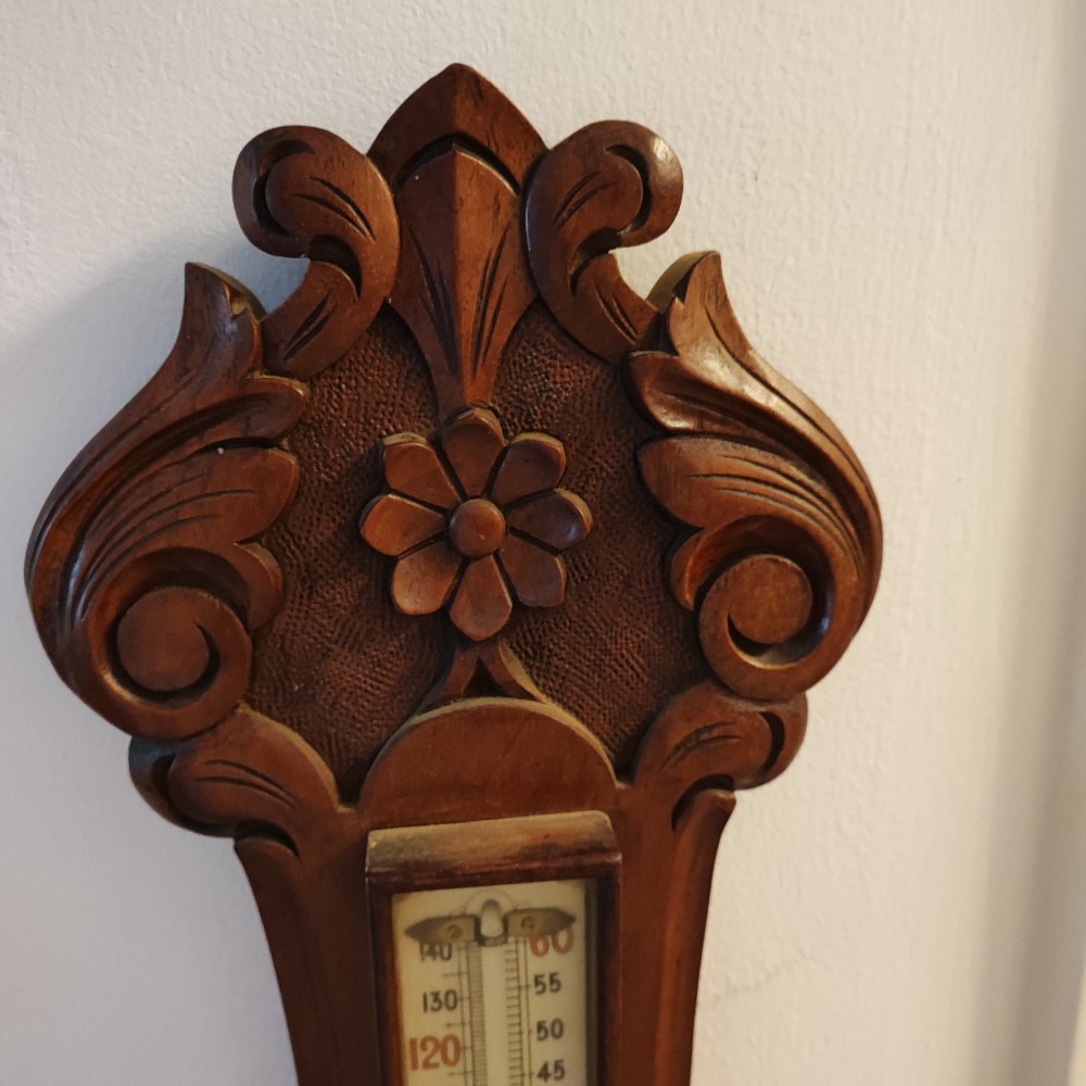 A carved Victorian mahogany aneroid wall barometer featuring top scrollwork, an integrated thermometer trunk, and a circular brass-rimmed dial. View VI
