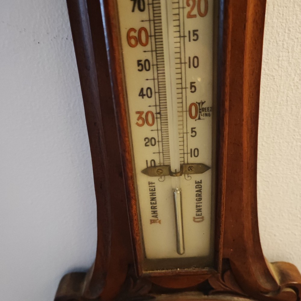 A carved Victorian mahogany aneroid wall barometer featuring top scrollwork, an integrated thermometer trunk, and a circular brass-rimmed dial. View VII