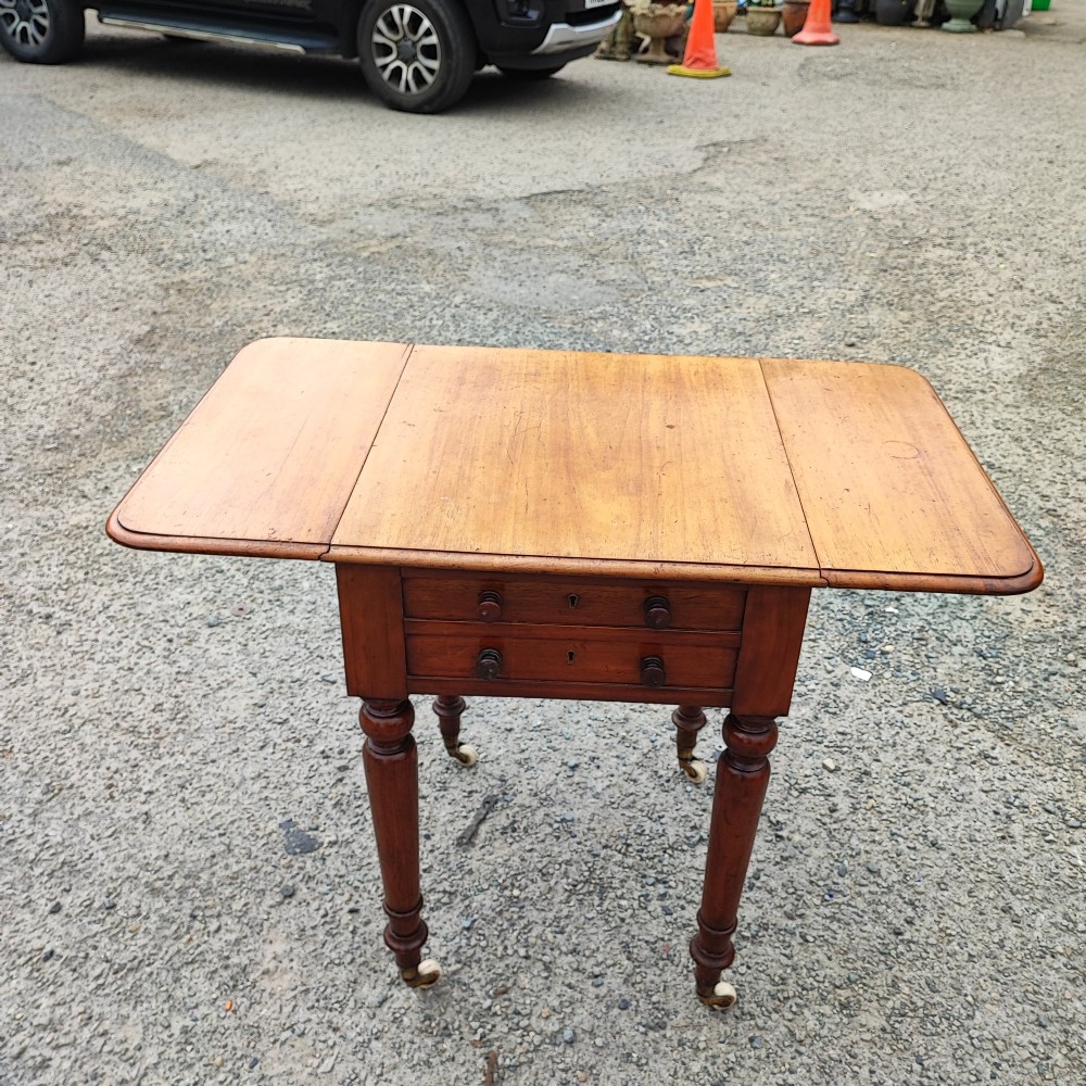 A warm brown mahogany Pembroke table featuring two drop-down leaves, two front drawers with round knobs, and turned legs fitted with castors. View II