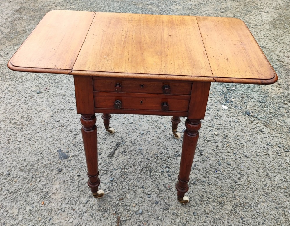 A warm brown mahogany Pembroke table featuring two drop-down leaves, two front drawers with round knobs, and turned legs fitted with castors. View III