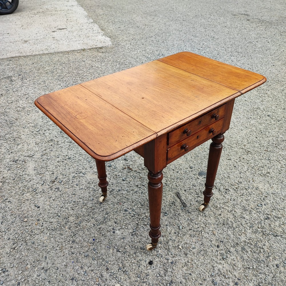 A warm brown mahogany Pembroke table featuring two drop-down leaves, two front drawers with round knobs, and turned legs fitted with castors. View IV
