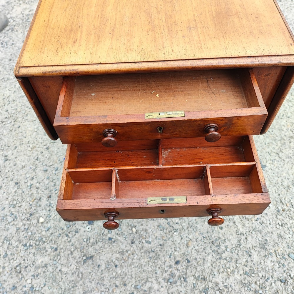 A warm brown mahogany Pembroke table featuring two drop-down leaves, two front drawers with round knobs, and turned legs fitted with castors. View V