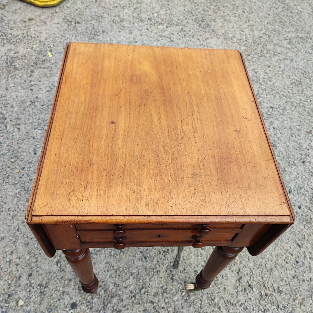 A warm brown mahogany Pembroke table featuring two drop-down leaves, two front drawers with round knobs, and turned legs fitted with castors. View X
