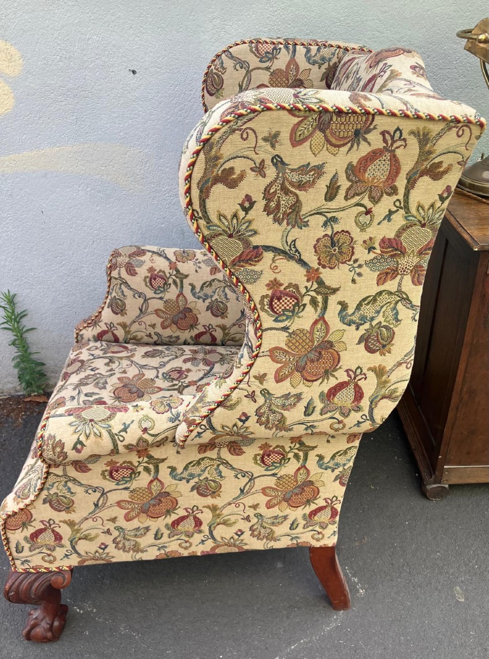 A high-back wing chair featuring floral tapestry upholstery, rolled arms, braided edge trim, and carved mahogany cabriole front legs with ball and claw feet. View VI