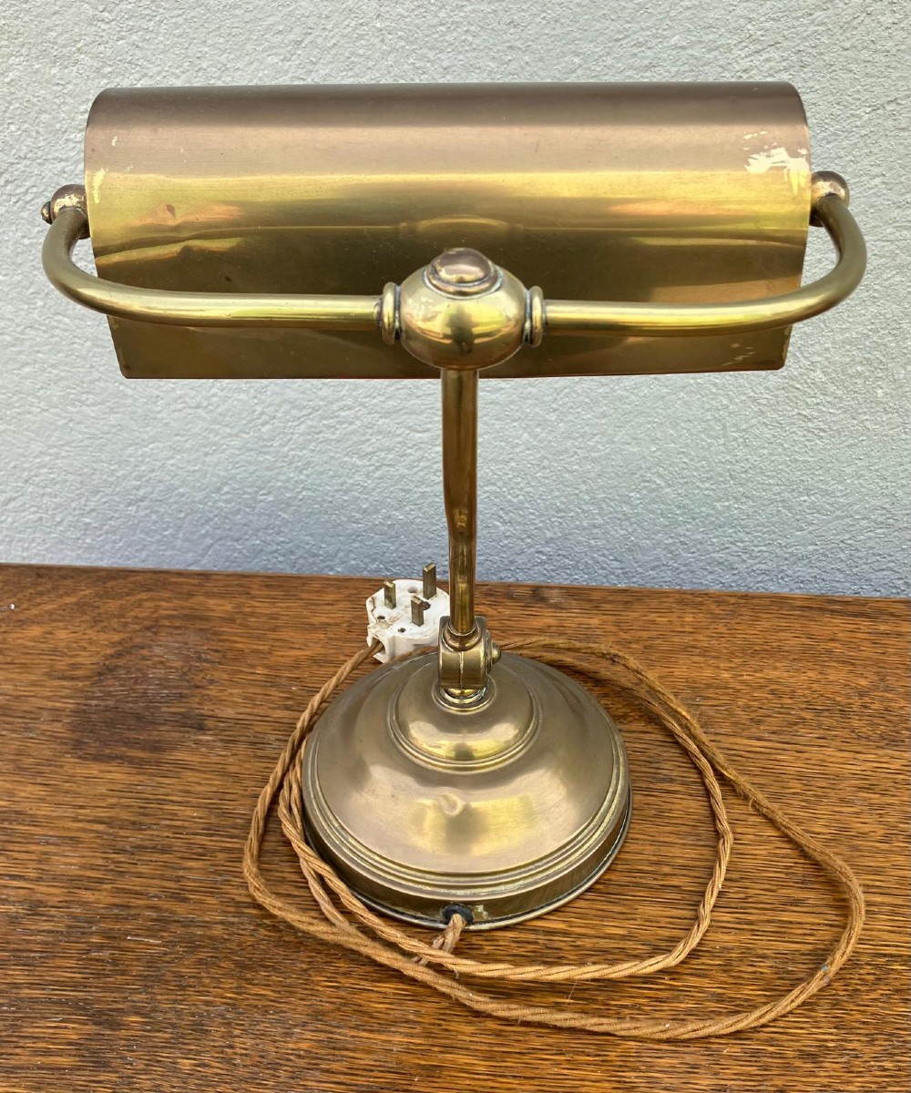 An antique brass desk lamp featuring a curved adjustable arm, a weighted stepped base, and a pivoting brass shade. View IV