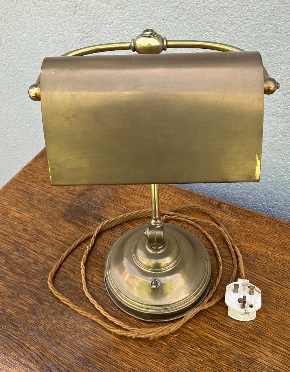 An antique brass desk lamp featuring a curved adjustable arm, a weighted stepped base, and a pivoting brass shade. View VI