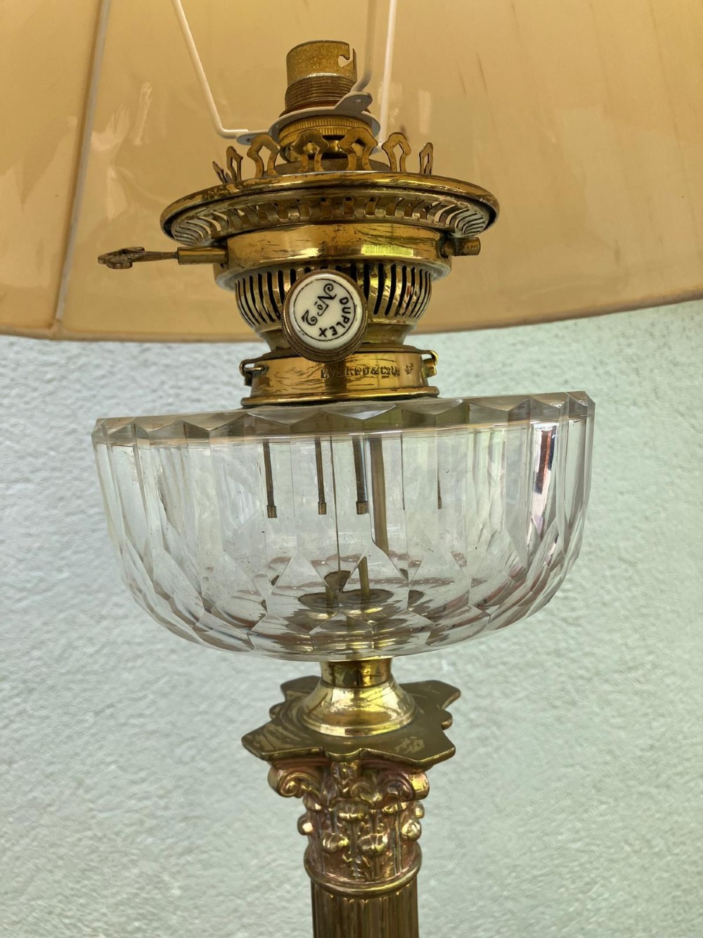An antique brass table lamp featuring a fluted Corinthian column stem, cut-glass reservoir, stepped pedestal base, and neutral cream lampshade. View II