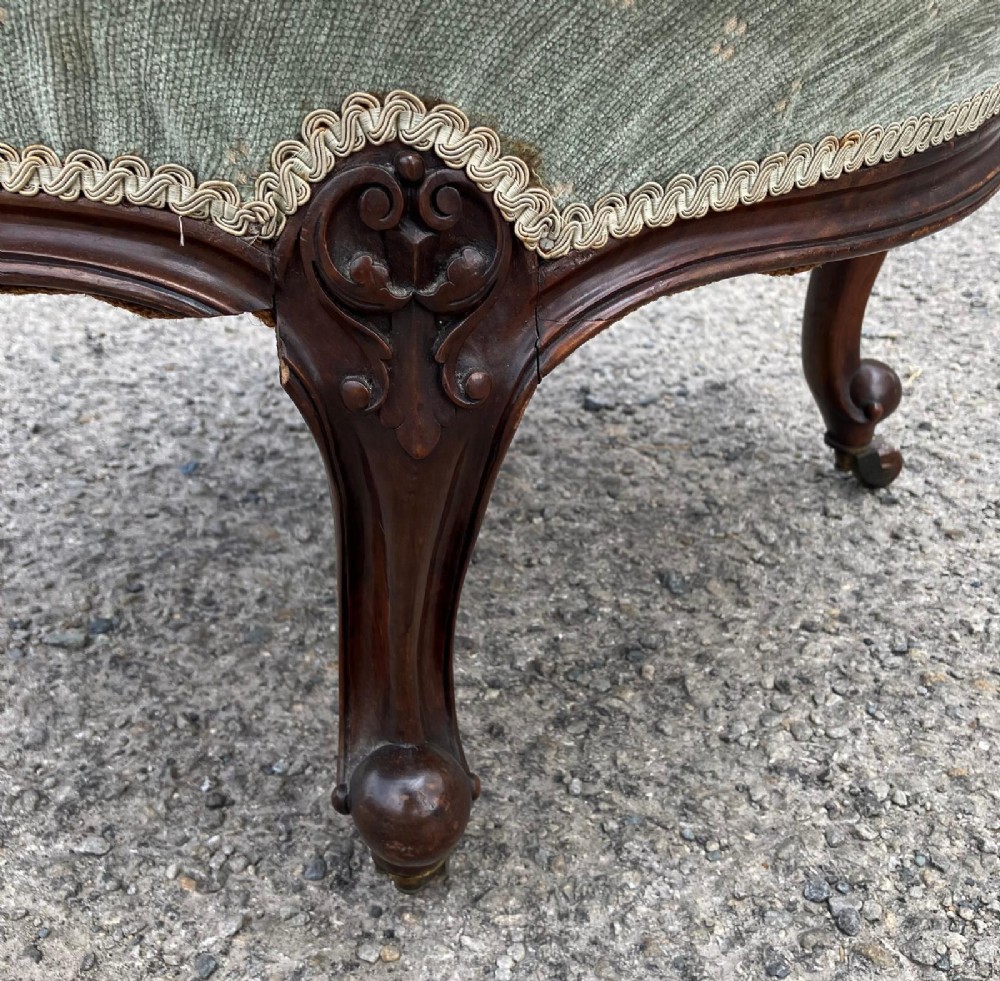 Victorian nursing chair featuring a carved walnut frame, sage green button-backed upholstery, and cabriole legs on brass castors. View II