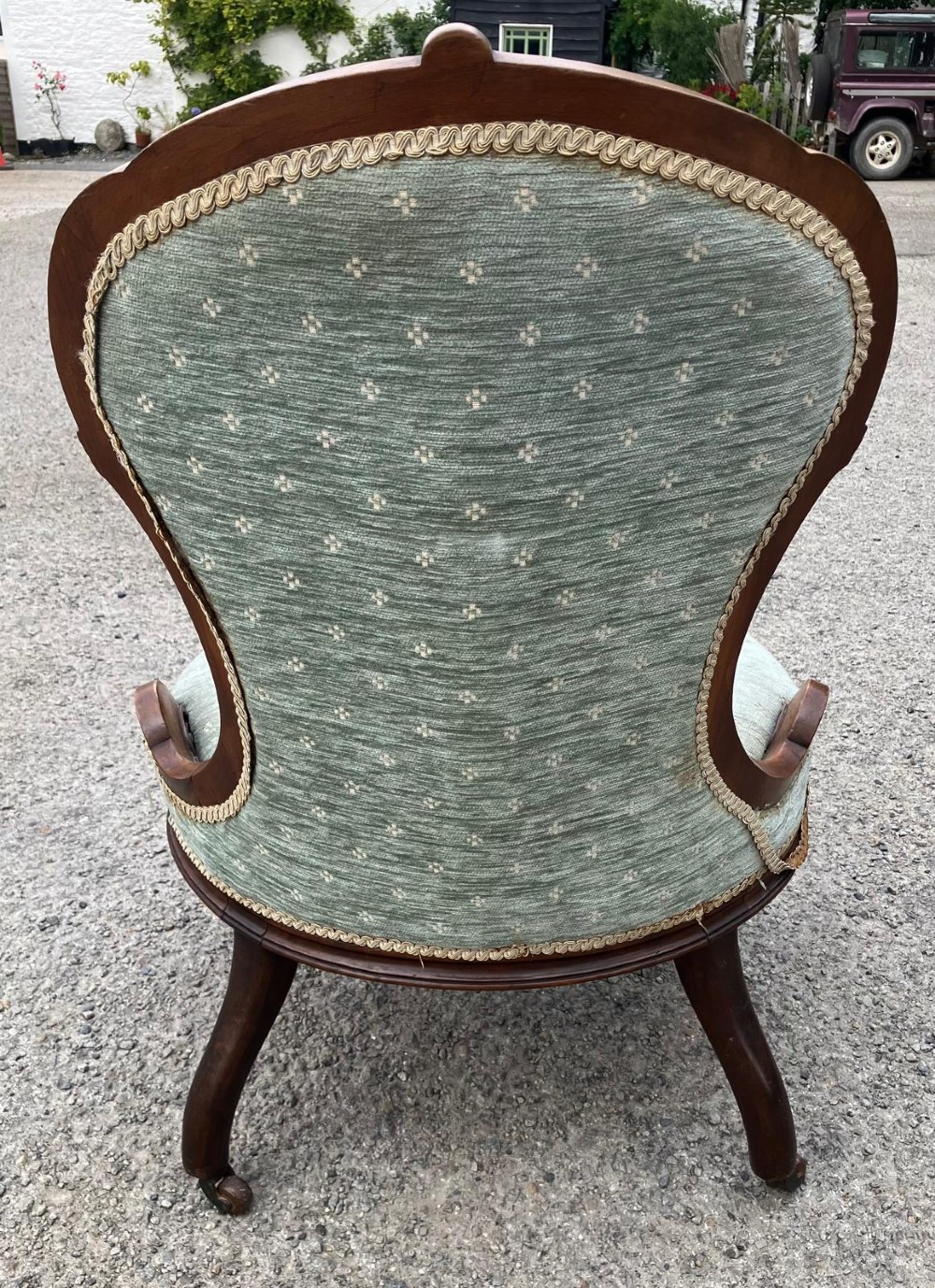 Victorian nursing chair featuring a carved walnut frame, sage green button-backed upholstery, and cabriole legs on brass castors. View IV
