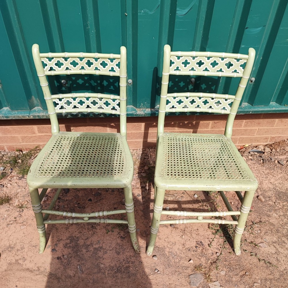 A pair of pale green painted side chairs featuring faux bamboo turned wooden frames, latticework backrests, and woven cane seats.