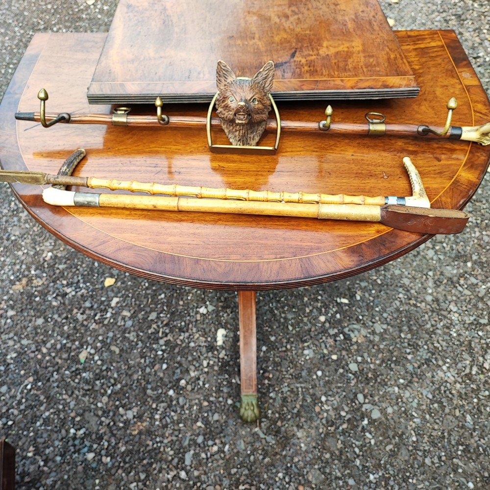 A carved wooden fox head whip rack mounted inside a brass stirrup frame with horizontal brass hooks on a wooden shaft.