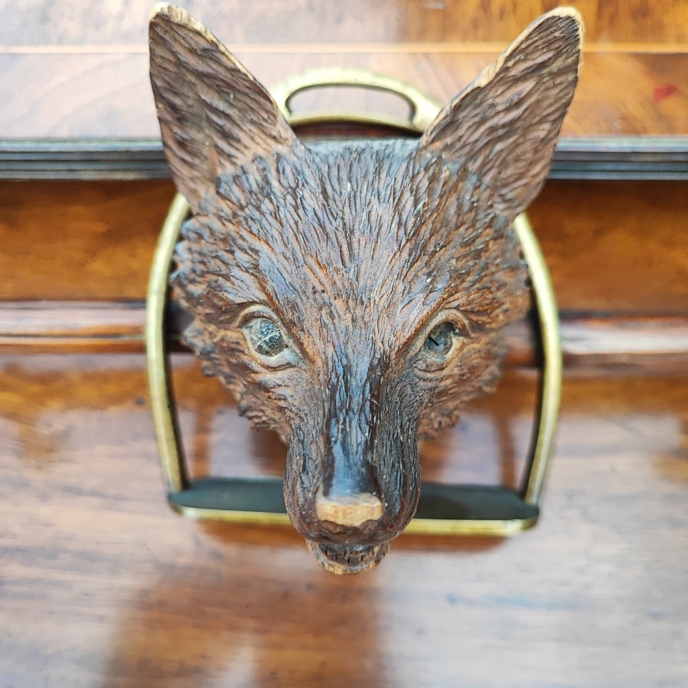 A carved wooden fox head whip rack mounted inside a brass stirrup frame with horizontal brass hooks on a wooden shaft. View II