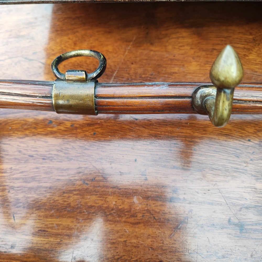 A carved wooden fox head whip rack mounted inside a brass stirrup frame with horizontal brass hooks on a wooden shaft. View V