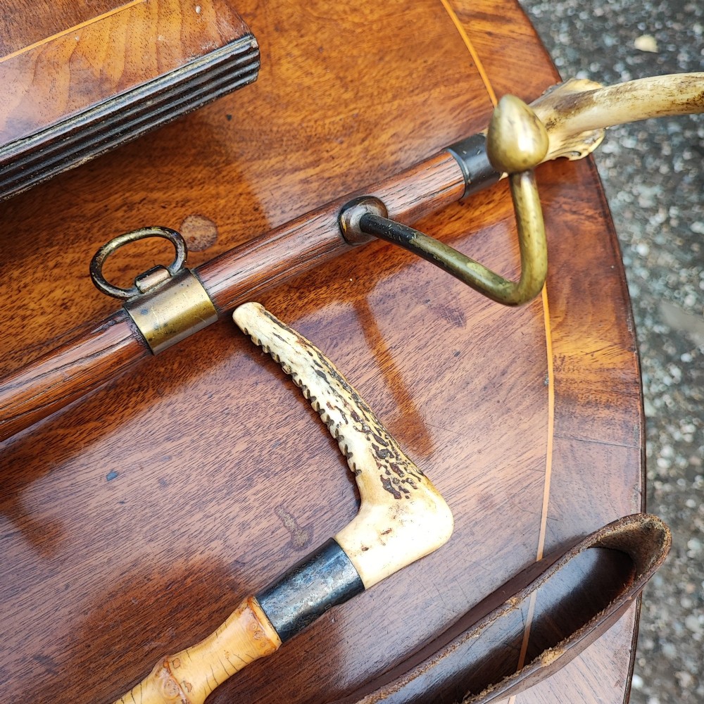 A carved wooden fox head whip rack mounted inside a brass stirrup frame with horizontal brass hooks on a wooden shaft. View VII