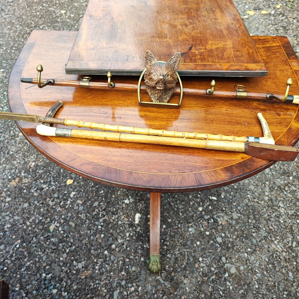 A carved wooden fox head whip rack mounted inside a brass stirrup frame with horizontal brass hooks on a wooden shaft. View VIII