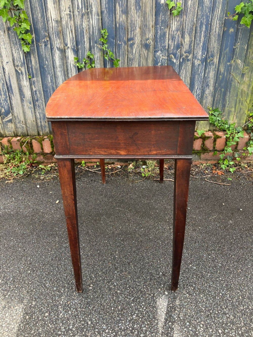 A Georgian bow-fronted mahogany side table featuring a single drawer with two brass handles and supported on four square tapered legs. View IV
