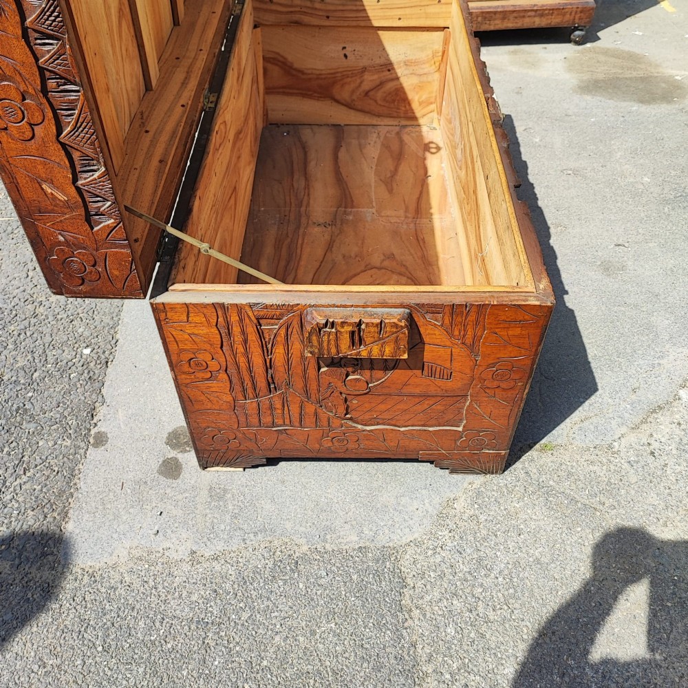 A relief-carved camphor wood trunk with relief panel depictions of figures on horseback and a central brass clasp. View IV
